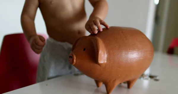 Child saving money adding coins inside piggy bank