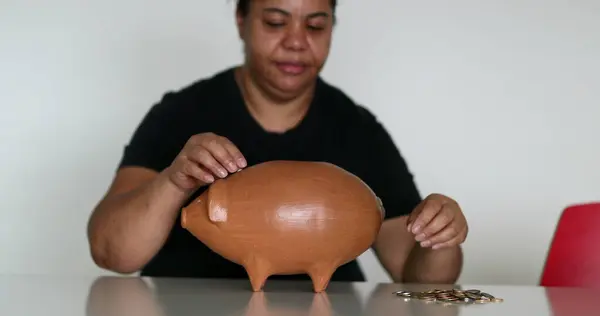 Black woman putting coins inside piggy bank, saving money concept