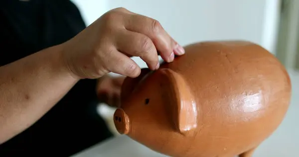 Close-up black person hands putting coins inside piggy bank