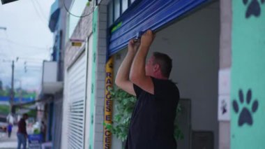 Şehir kaldırımındaki dükkan önünü kapatan adam. İnsan caddede dükkan vitrininde slayt yapar