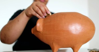 Close-up black person hands putting coins inside piggy bank