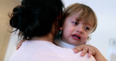 Tearful baby boy. Mother wearing surgical mask holding upset crying infant