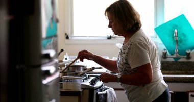 Senior woman cooking at home, casual candid older person stirring pot