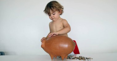 Adorable baby boy adding savings inside piggy bank