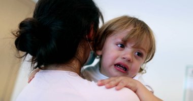 Tearful baby boy. Mother wearing surgical mask holding upset crying infant