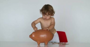 Little boy adding money in the bank for future investment. Toddler putting coins inside piggy bank
