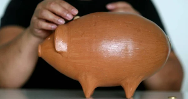 Close-up black person hands putting coins inside piggy bank