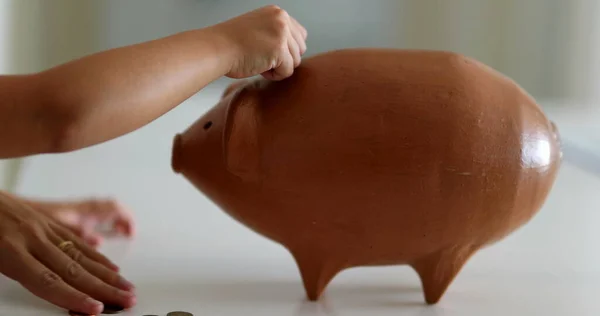 Close-up hands adding coins inside piggy bank investment