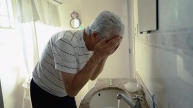 Yaşlı bir adam banyo aynası önünde dişlerini fırçalıyor, günlük sabah ritüeli, yaşlılıkta ev hayatını tasvir ediyor.