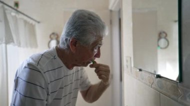 Yaşlılık sabahı rutininde banyo aynasının önünde dişlerini fırçalayan kıdemli bir adam. Güne yaşlı, beyaz saçlı biri başlıyor.