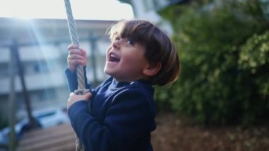 Neşeli Çocuğun Yürek ısıtan Yakın Çekimi Ağaçlar Arasındaki İpte Kayıyor, Nostaljik Park Eğlencesi. Genç çocuk sıkıca sarıldı ve aşağı doğru kayıyor.
