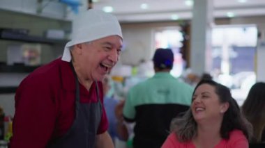 Müşterilerle gülen ve restoran kafeteryasının içinde yemek siparişlerini yazan neşeli kıdemli garson.