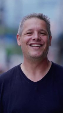 Mutlu orta yaşlı adam kameraya bakıp gülümsüyor ve gülümsüyor. Dikey Video