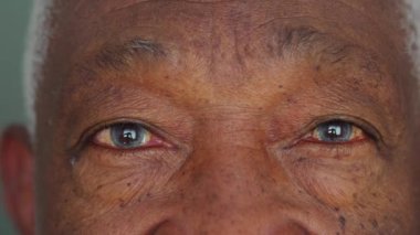 Tarafsız bir ifadeyle yaşlı siyah bir adamın makro yakın çekimi, mavi gözlü detay yüzü.