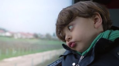 Trenle seyahat eden sıkılmış bir çocuk, seyahat ederken ya da seyahat ederken can sıkıntısı çeken bir çocuğun yakın çekim yüzü.