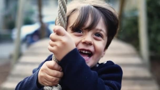 无忧无虑的小男孩紧紧抓住绳子 滑落在两棵树之间的铁丝上 激起了幸福的概念 快乐孩子的近照 — 图库视频影像