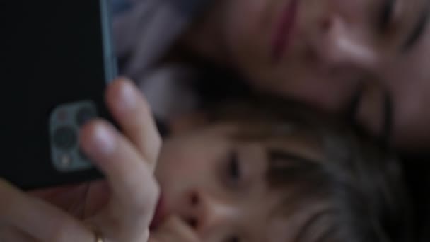 母亲和孩子近距离地看着放在床上的手机装置屏风 父母和儿子被网上娱乐内容所吸引 — 图库视频影像