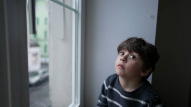 Sıkılmış küçük bir çocuk pencerenin kenarında oturup dışarı çıkmak istiyor. Sonbahar soğuğu mevsiminde sıkıntıdan patlayan bir çocuk.