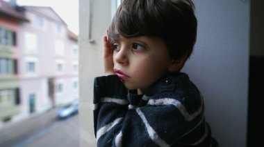 Sıkılmış bir çocuk pencereden dışarı bakıyor, küçük bir çocuk dışarı çıkmak istiyor. Yapacak bir şeyi olmayan üzgün çocuk, ikinci kattan sokağa bakıyor.