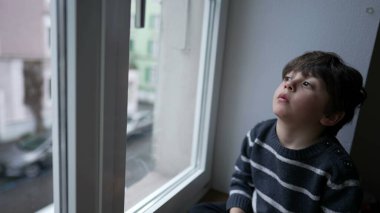 Sıkılmış küçük bir çocuk pencerenin kenarında oturup dışarı çıkmak istiyor. Sonbahar soğuğu mevsiminde sıkıntıdan patlayan bir çocuk.