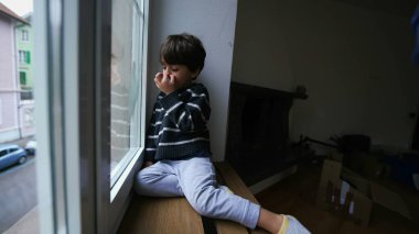 Evde pencerenin kenarında oturan çocuk burnunu karıştırıyor. Evden dışarı bakıyor. Sıkıcı küçük çocuk içeride kilitli.