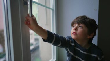 Pencere tokmağı tutan küçük bir çocuk ikinci kat penceresini açmak istiyor. Çocuğun güvenlik endişeleri, güvenlik önlemleri.