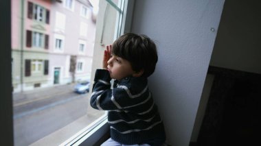 Sıkılmış bir çocuk pencereden dışarı bakıyor, küçük bir çocuk dışarı çıkmak istiyor. Yapacak bir şeyi olmayan üzgün çocuk, ikinci kattan sokağa bakıyor.