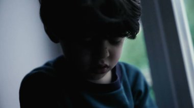 Üzgün bunalımlı çocuk karanlık, kasvetli, melankolik küçük çocuk pencerenin önünde oturuyor.