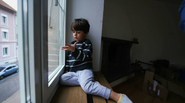 Evde pencerenin kenarında oturan çocuk burnunu karıştırıyor. Evden dışarı bakıyor. Sıkıcı küçük çocuk içeride kilitli.