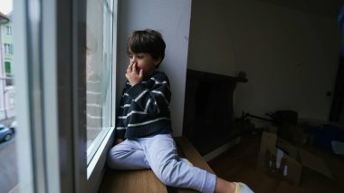 Evde pencerenin kenarında oturan çocuk burnunu karıştırıyor. Evden dışarı bakıyor. Sıkıcı küçük çocuk içeride kilitli.