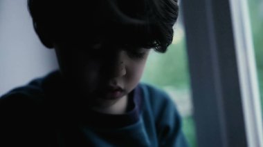 Üzgün bunalımlı çocuk karanlık, kasvetli, melankolik küçük çocuk pencerenin önünde oturuyor.