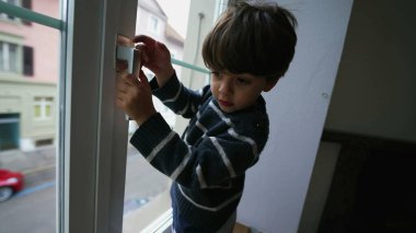 Pencere koluna tutunan bir çocuk. İkinci kattaki apartmanın camının yanındaki küçük çocuk tehlikesi.