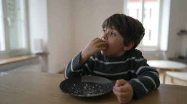 Küçük çocuk bir parça ekmek yiyor, yakın plan 4 yaşında çocuk karbonhidrat yiyor, masada oturuyor.