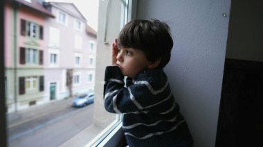 Sıkılmış bir çocuk pencereden dışarı bakıyor, küçük bir çocuk dışarı çıkmak istiyor. Yapacak bir şeyi olmayan üzgün çocuk, ikinci kattan sokağa bakıyor.
