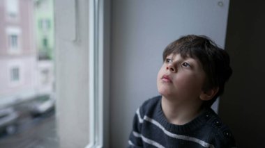 Sıkılmış küçük bir çocuk pencerenin kenarında oturup dışarı çıkmak istiyor. Sonbahar soğuğu mevsiminde sıkıntıdan patlayan bir çocuk.