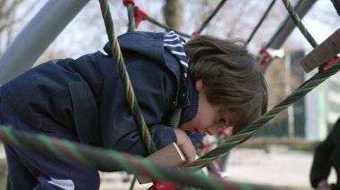 Çocukların kış mevsiminde çocuk parkına tırmanırken üzerinde kalın bir ceket vardı. Çalışkan küçük çocuk halatı tutuyor ve dışarıda egzersiz yapıyor.