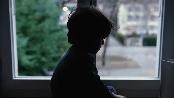 stock image Melancholic child sitting by window at home feeling sad and depressed