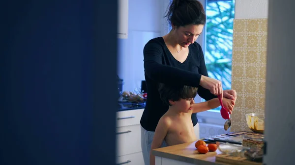 Candid mother and child cooking at home, preparing pastry food together in authentic real life parenting domestic scene