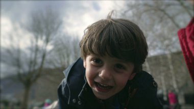 Heyecanlı çocuk, sonbahar mevsiminde oyun sahasında daireler çizerken gülümsüyor, küçük çocuğun yakın çekim yüzü heyecan ve mutluluğu hissediyor.