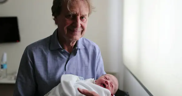 Grand-father smiling to camera while holding newborn baby
