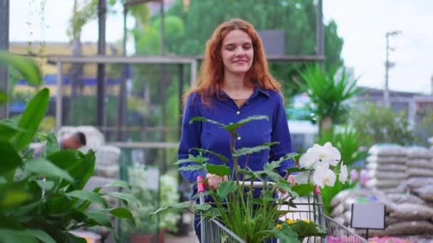 Радостная Женщина Покупает Растения Цветы Магазине Садоводства Рыжеволосая Женщина Синей — стоковое видео