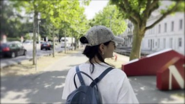 Sunny Solo Stroll - Atkuyruklu Cap Giyen Kadın ve Sırt Çantası Bustling Bulvarı ve Tarihi Bina