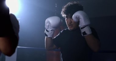 Ringin içinde boks eldiveni giyen genç adam yine yoğun bakışlar atıyor. Ağır çekimde dramatik ışıklandırmayla yakalanan rakip.