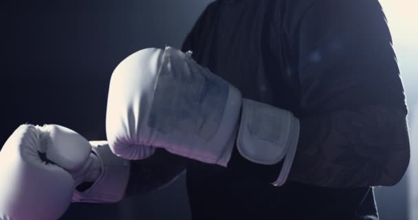 ボクシンググローブを身に着けている男性のクローズアップは 劇的な照明でリングの中に立っています 戦闘の詳細機器 — ストック動画