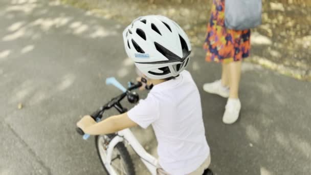 骑自行车成功 骑着头盔的男孩独立地骑着他的装备自行车在他的父母前面的黑暗人行道上 — 图库视频影像