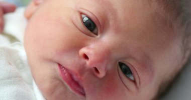 Newborn baby face looking to camera after birth, curious infant