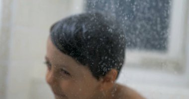 Damlacıklar yavaş çekimde akıyor. Arka planda bulanık bir çocuk var. Küçük çocuk, rüya gibi bir sahnede banyo yaparken cesedi yıkıyor.