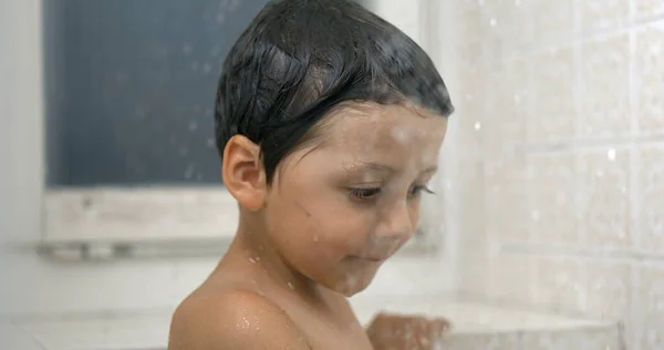 One small boy observing water droplets fall in super slow-motion standing in shower bath