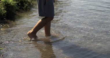 Çocuk bacakları ve ayakları kıyıdan göle giriyor. Doğanın tadını çıkarıyor, esir alınıyor.
