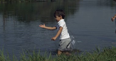 Göl kenarında su sıçratan küçük çocuk yakalandı. Doğanın tadını çıkaran çocuk doğayla iç içe.